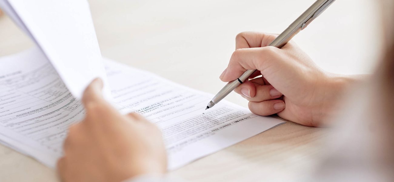 Crop shot of person with pen signing contract at desk in daylight