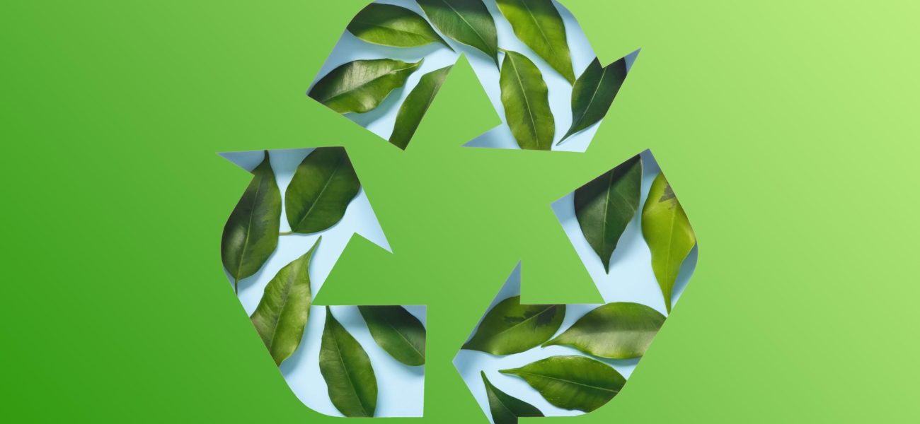 Recycle symbol made of cut paper and green leaves on blue background. Reuse, reduce, recycle concept.